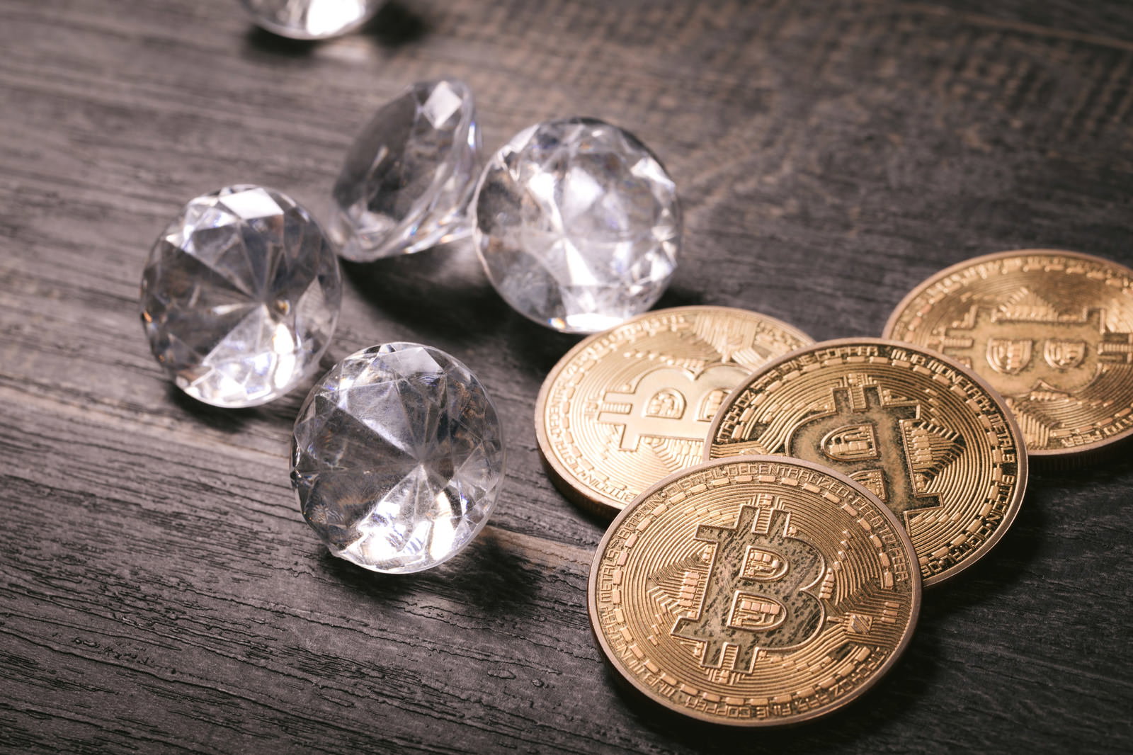 木目調のテーブルに置かれたビットコインの金貨と透明なダイヤモンド