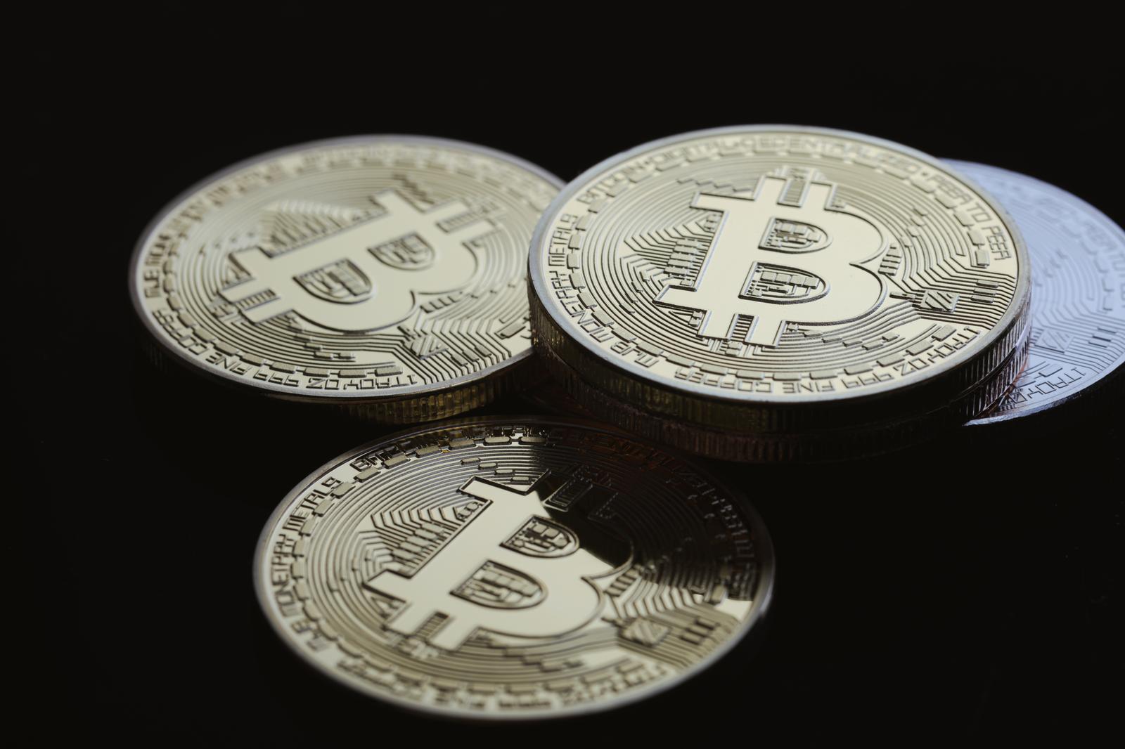 3枚の銀色ビットコインコインが黒い背景に積み重なっている
