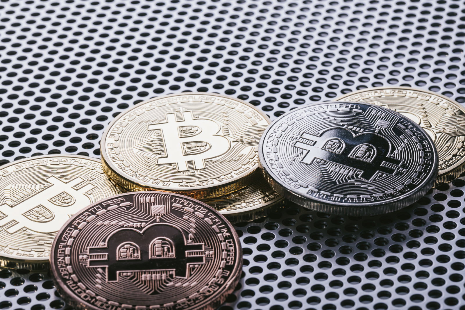 パンチングメタルの上に並ぶ金色・銀色・銅色のビットコインコイン