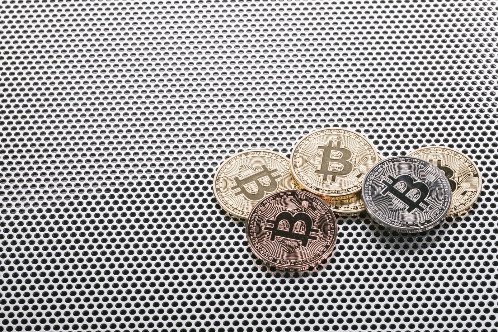 メタルメッシュの背景に配置された金色と銀色のビットコインコイン4枚