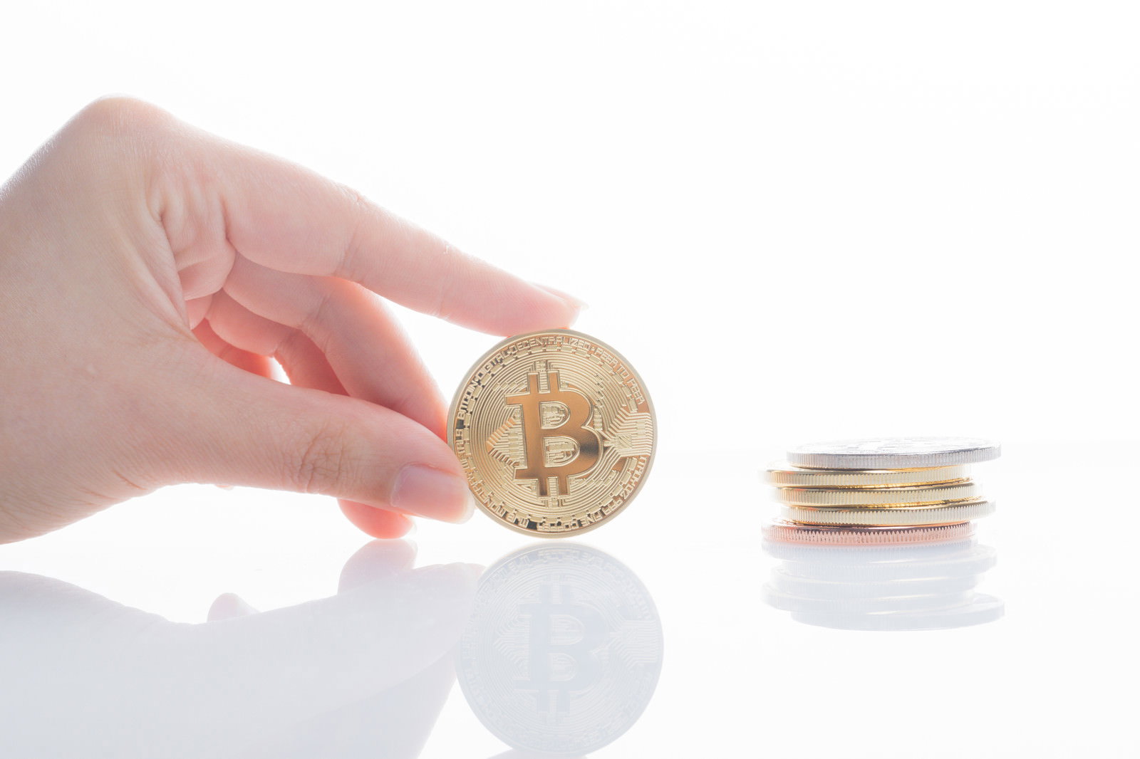 金色のビットコインコインを指でつまんで持つ手と積み重ねられたコイン