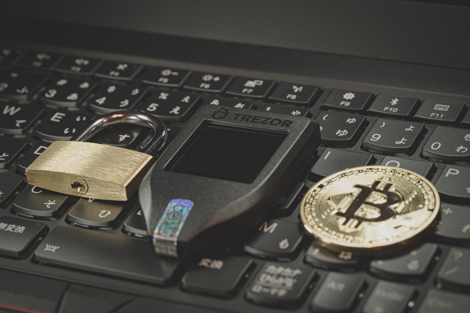 黒いキーボードの上に配置されたTrezor Model T、南京錠、ビットコイン