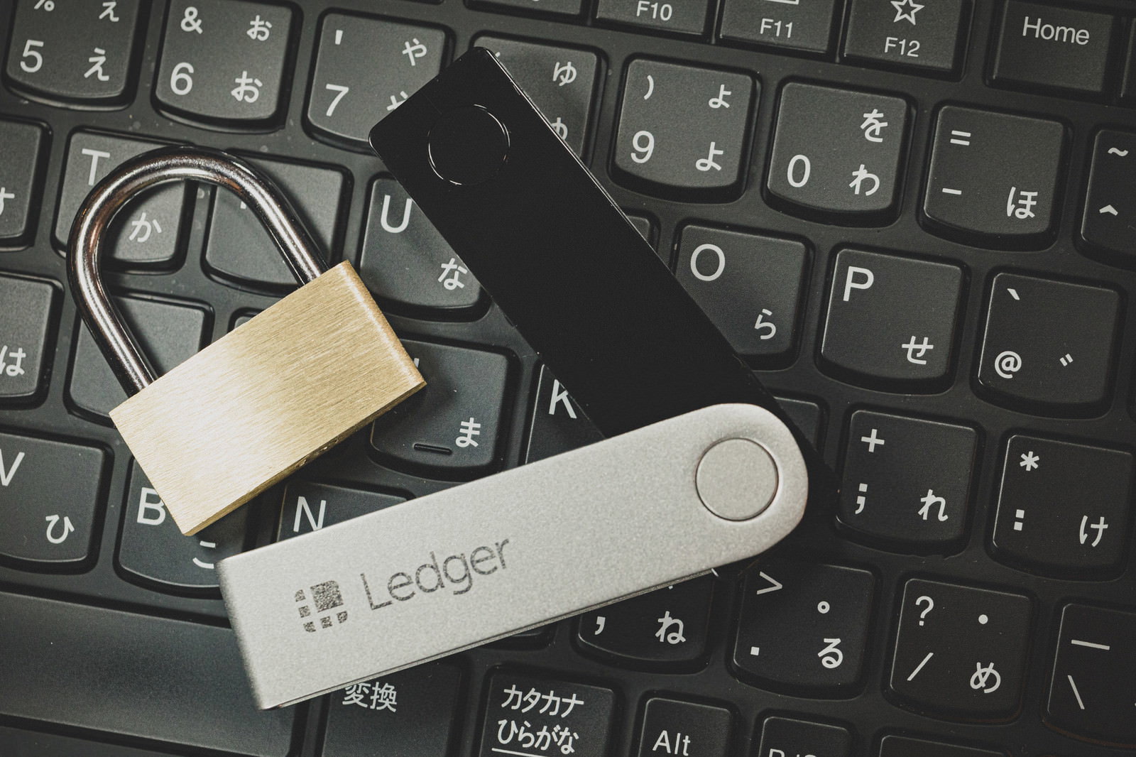 黒いキーボードの上に置かれた白い南京錠とLedger NANO S