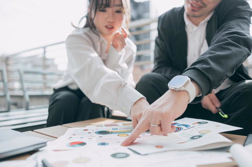 紙の資料に指をさしてグラフについて説明する上司と、その内容に驚く女子社員