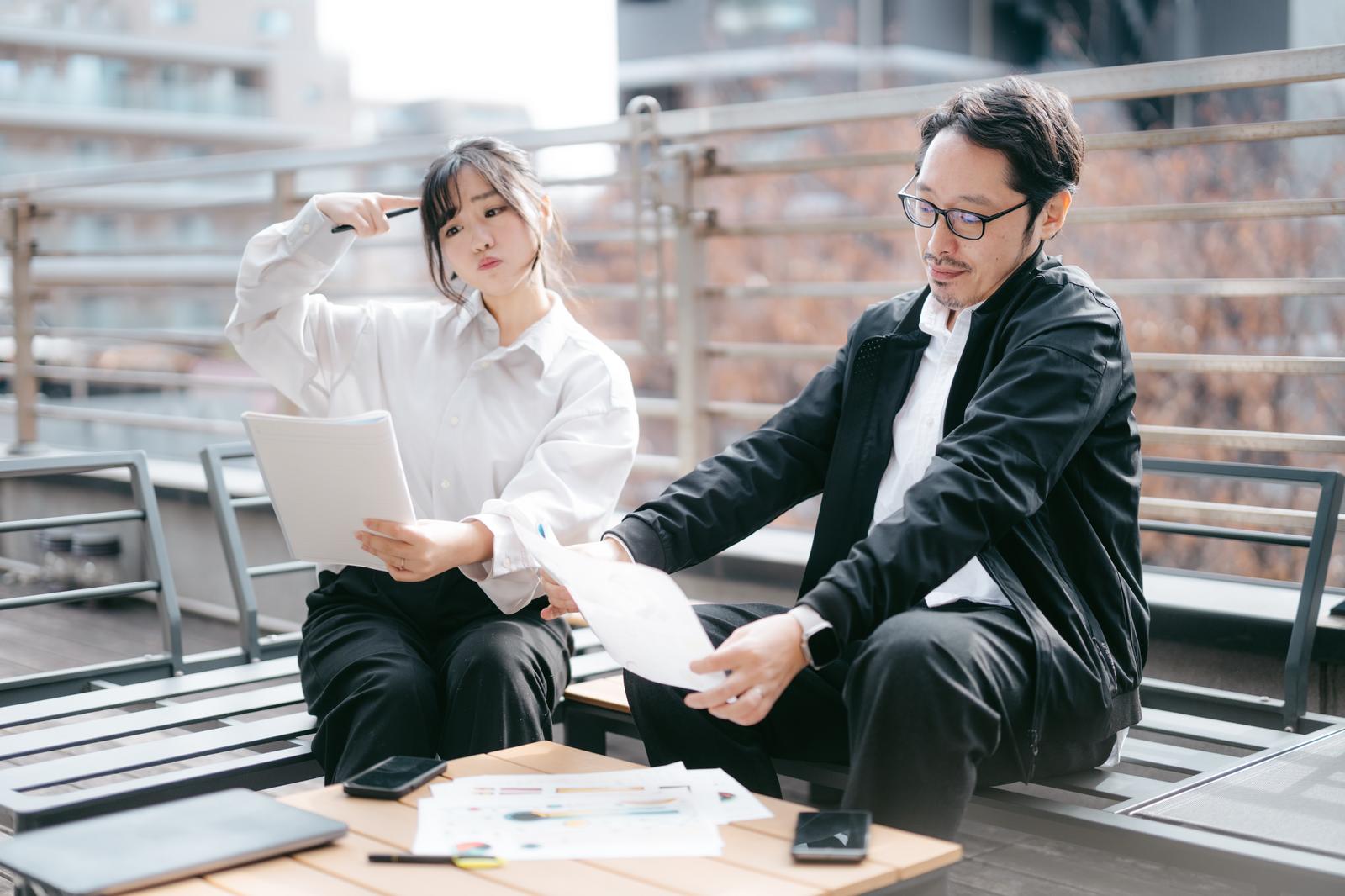 屋上でタブレットと資料を見ながら打ち合わせをする上司と女性スタッフ［モデル：河村友歌 ゆうせい］