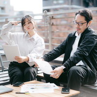 ビルの屋上で資料を見ながら打ち合わせをする上司と主任女子の写真