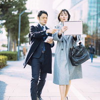 都市の歩道で資料を確認しながら打ち合わせする男性と女性の写真