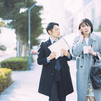 アポ無しで営業電話をかける女性の上司と不安そうな顔で見つめる外回りの男性社員の写真
