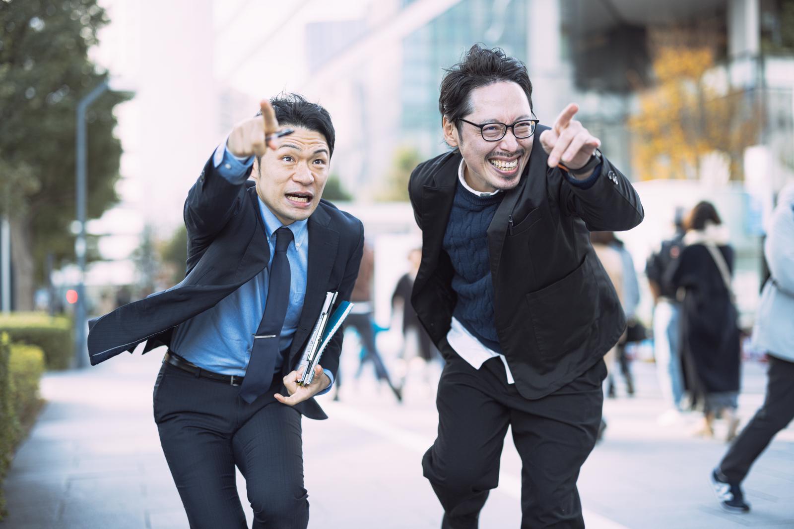 指をさしながらビジネス街を走る2人の営業マン［モデル：ゆうせい モデルリリース］