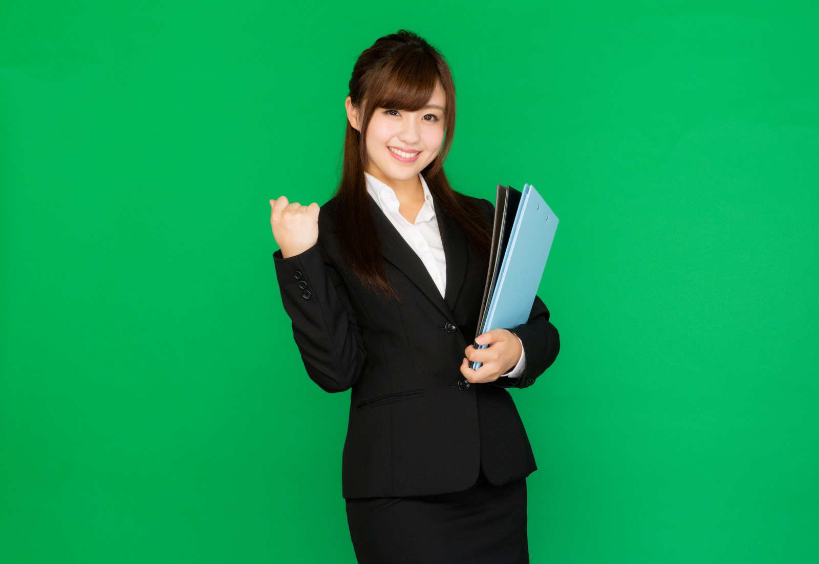 グリーンバック前でガッツポーズするスーツ姿の女性［モデル：河村友歌］