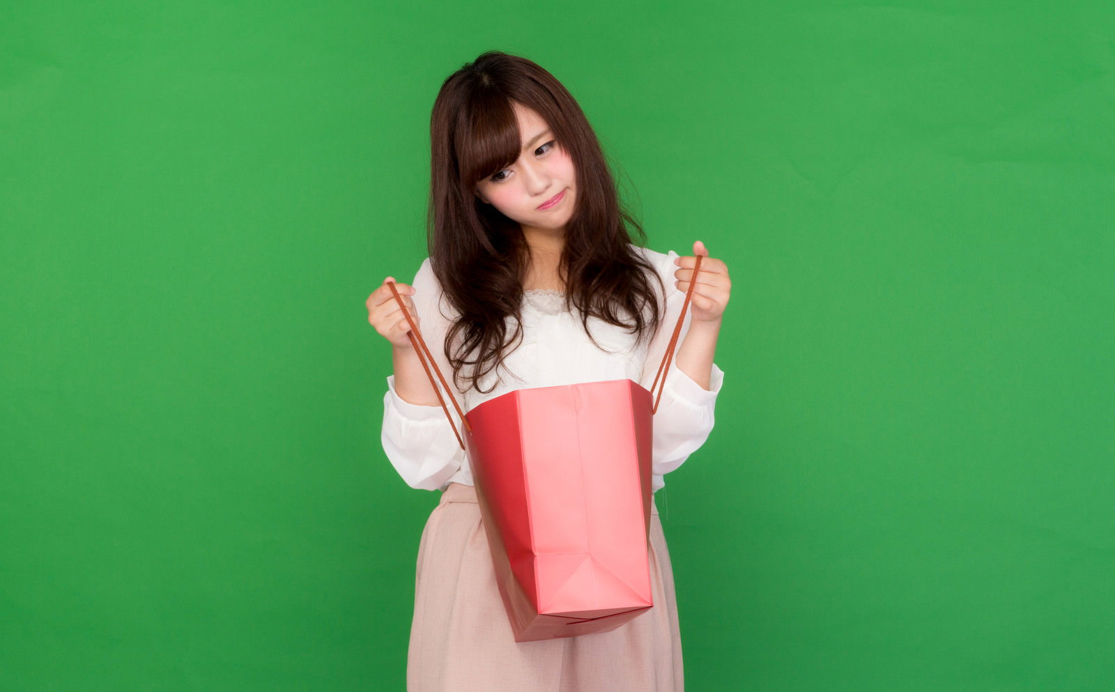 ピンクの買い物袋を持ってがっかりした表情の女性［モデル：河村友歌］