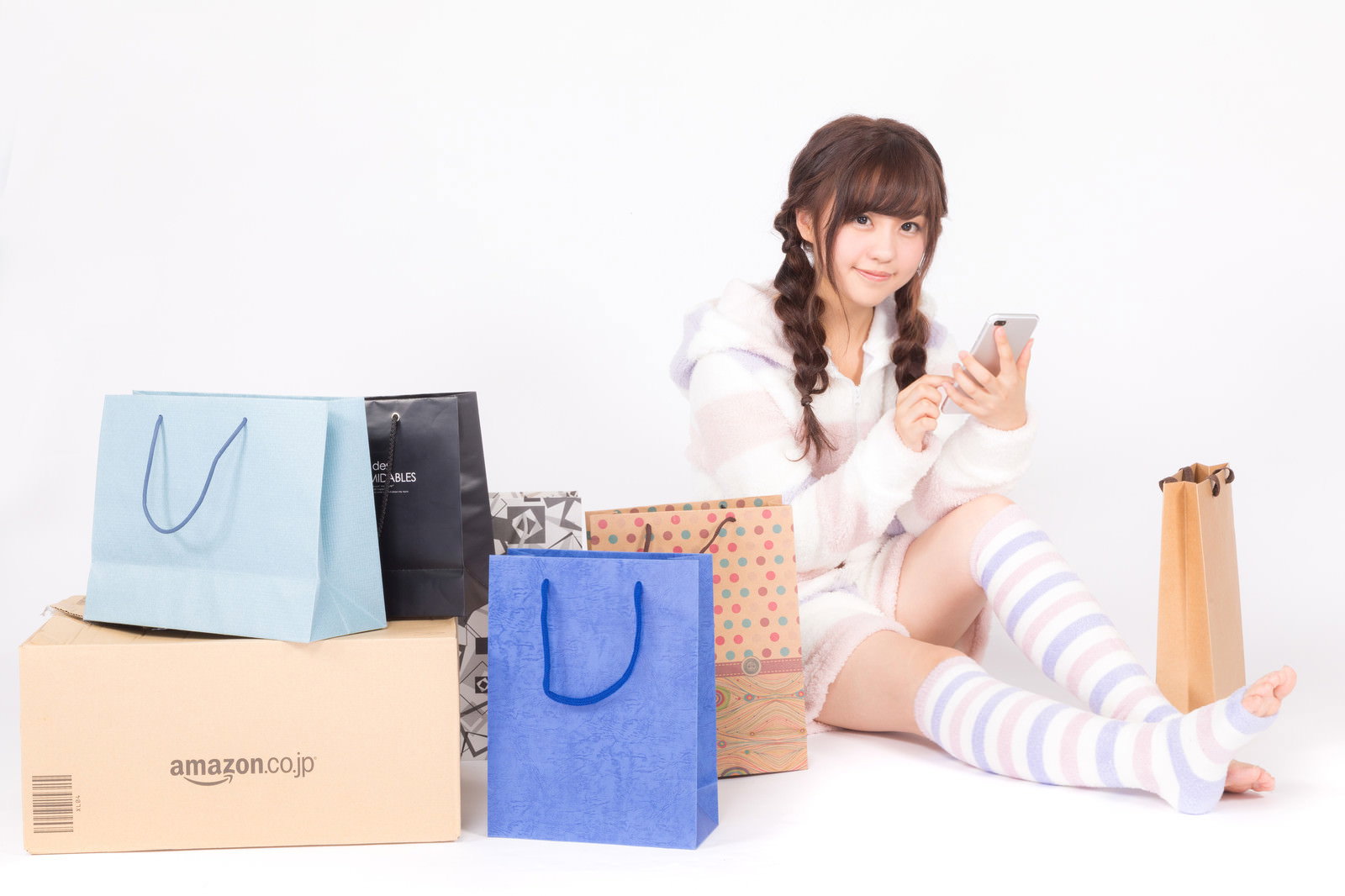 カラフルなショッピングバッグに囲まれてスマートフォンを手に持つ、白いニットの女性［モデル：河村友歌］