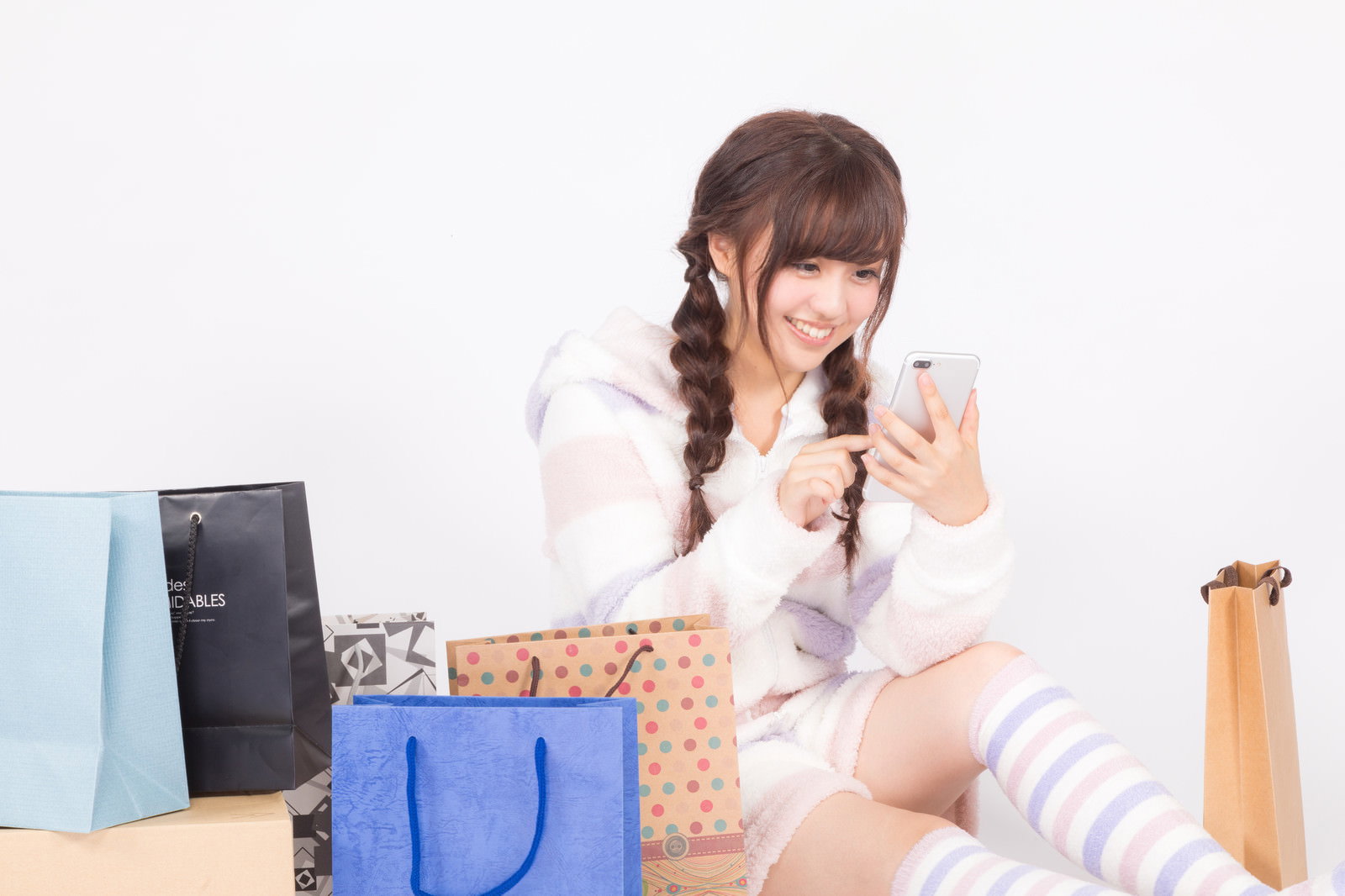 セール時期にスマートフォンを操作しながら複数の買い物袋に囲まれた女性の姿［モデル：河村友歌］