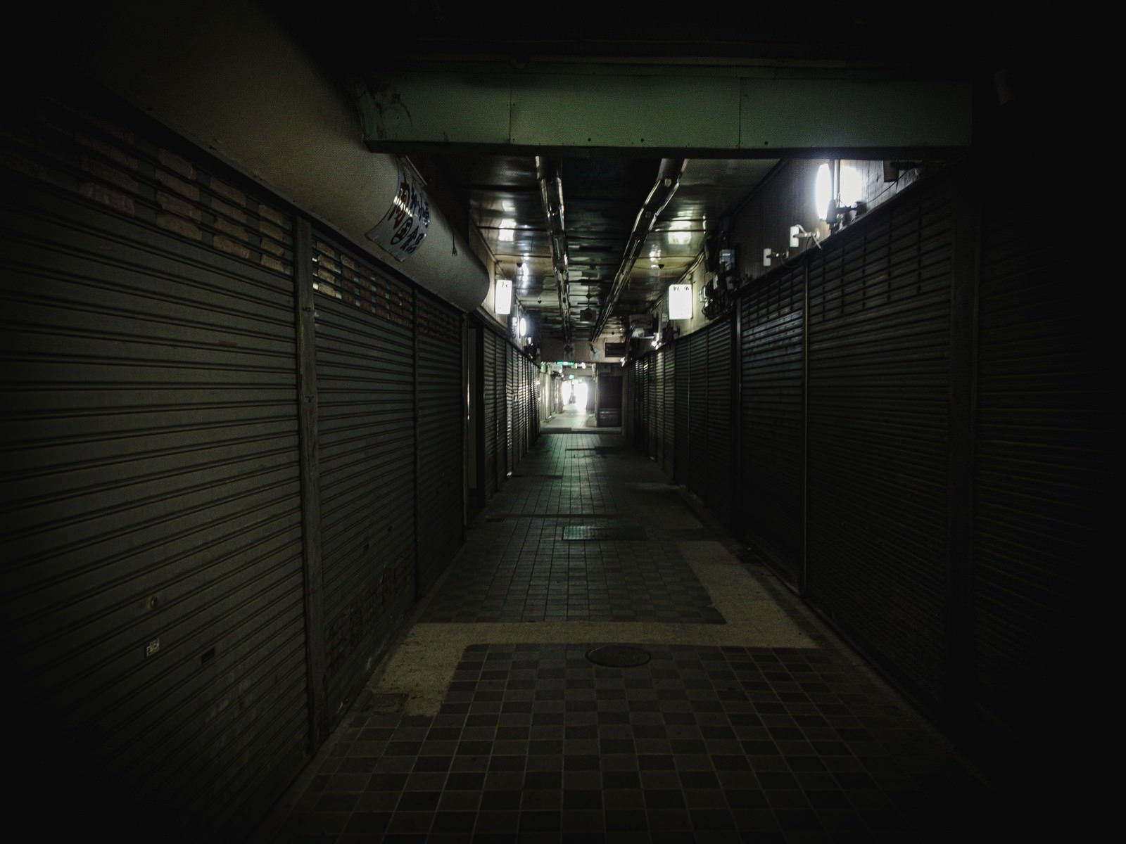 夜の商店街でシャッターが閉まった店舗が並ぶ薄暗い通路
