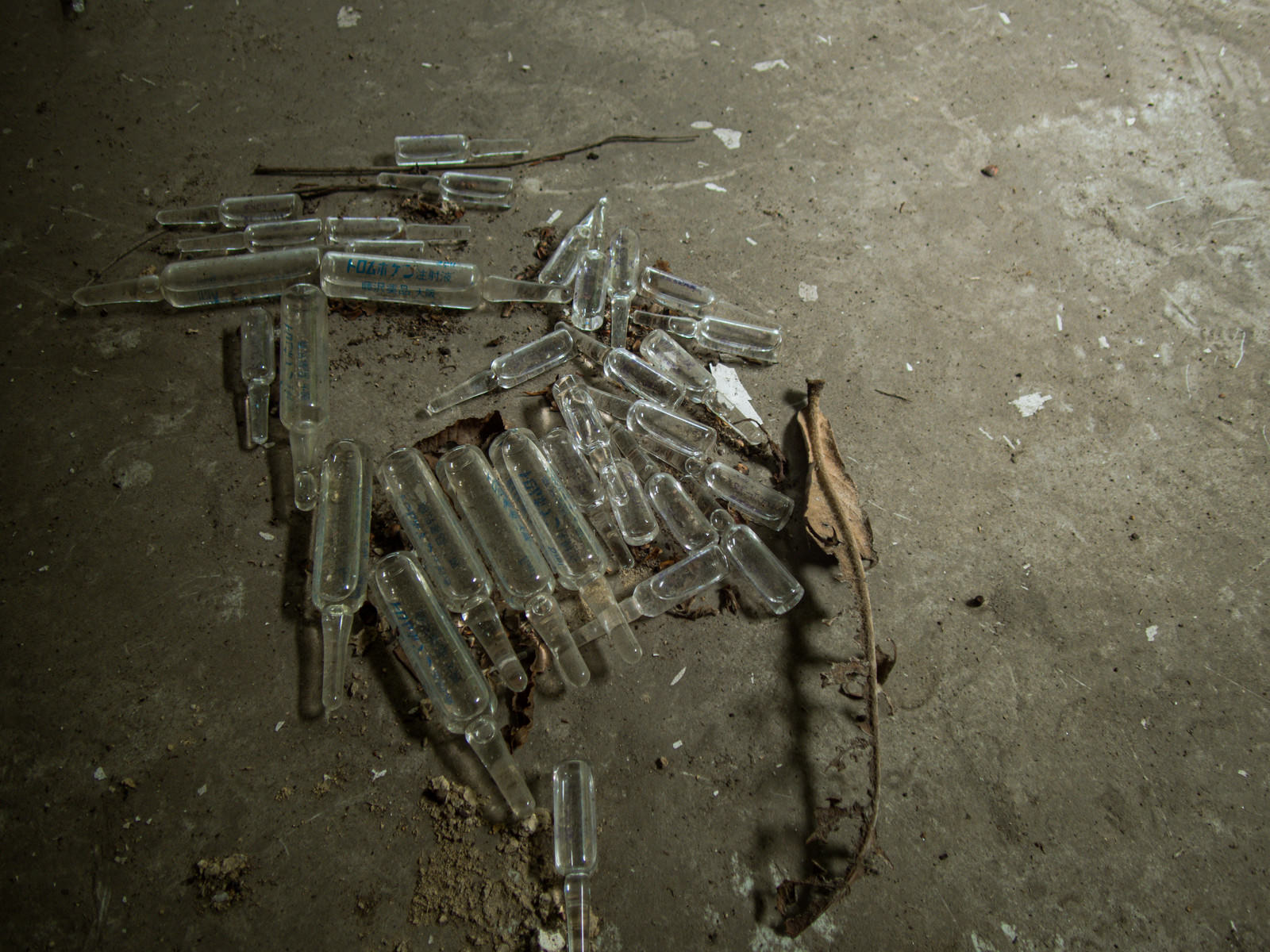 廃墟のコンクリート床に散らばる割れた注射液用瓶のガラス片