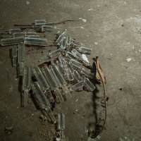 廃墟に散らばる注射液用瓶の残骸とガラス片の写真