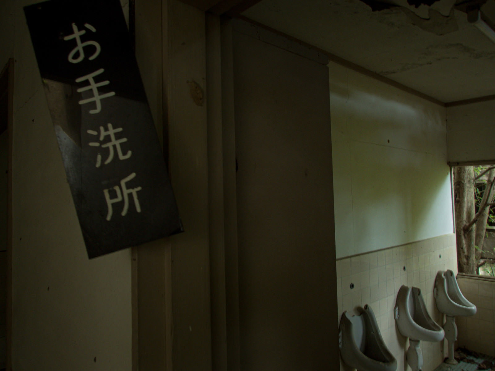 薄暗い廃墟内にある緑色の看板にお手洗い所と書かれたトイレの入り口