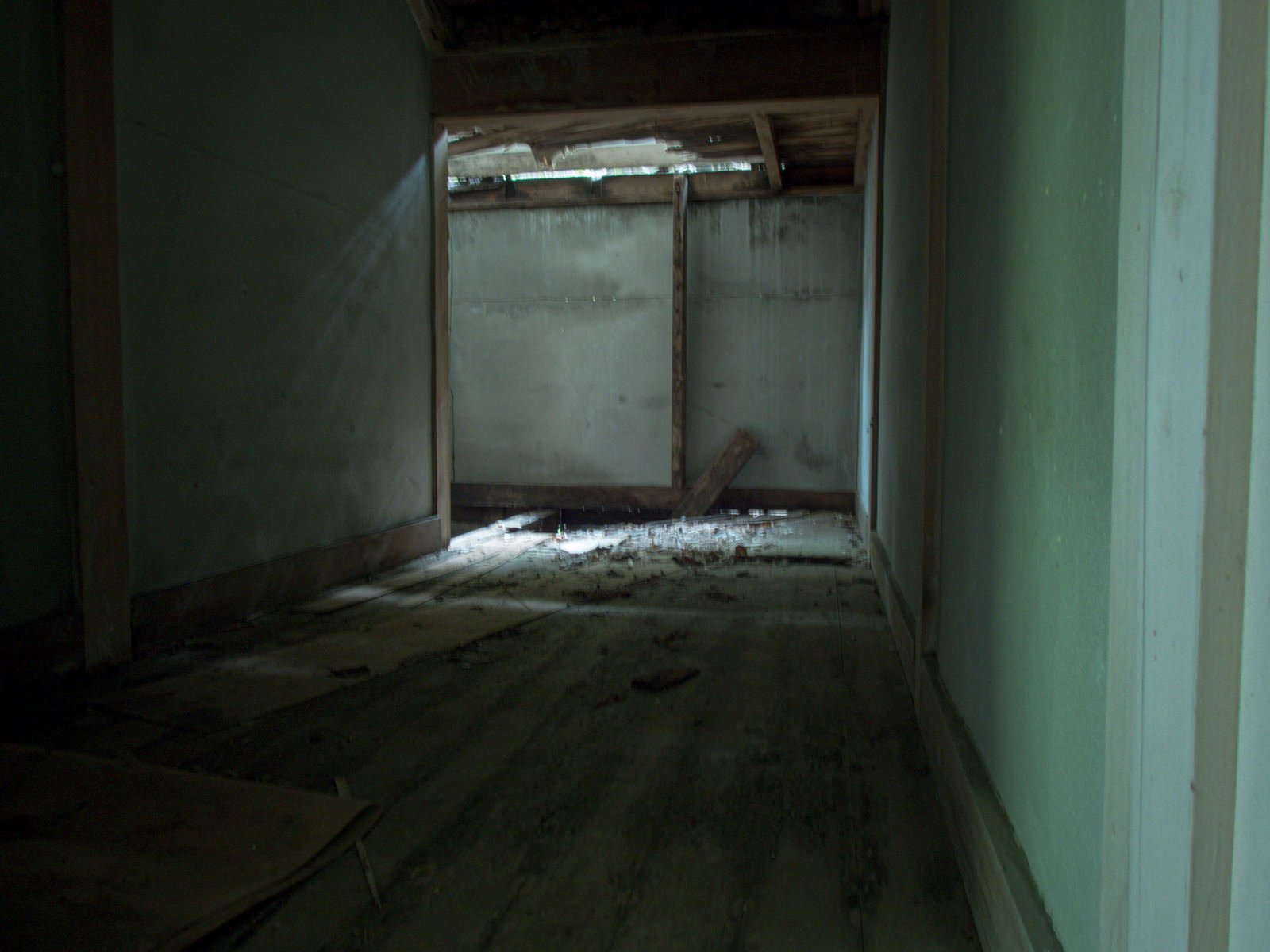 崩落した天井から光が差し込む廃屋の室内