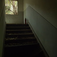 廃墟の階段の上に設置された赤い消化器と老朽化した壁の写真