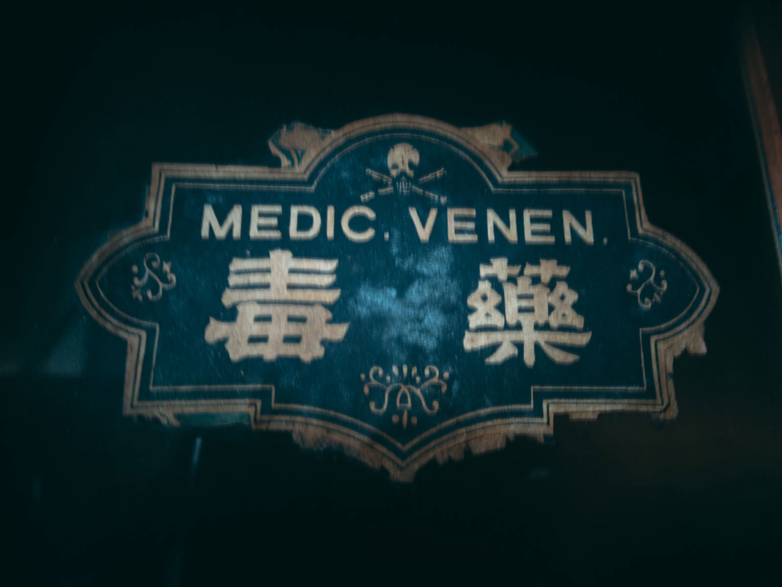 暗い背景に緑色で「MEDIC VENEN」と「毒薬」と書かれたエンブレム