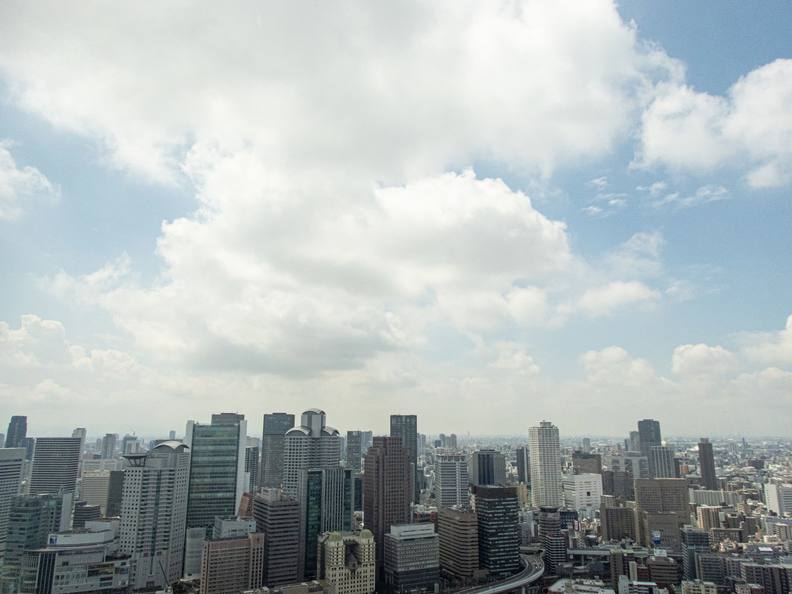 白い雲が浮かぶ青空の下に高層ビル群が立ち並ぶ大阪梅田の街並み