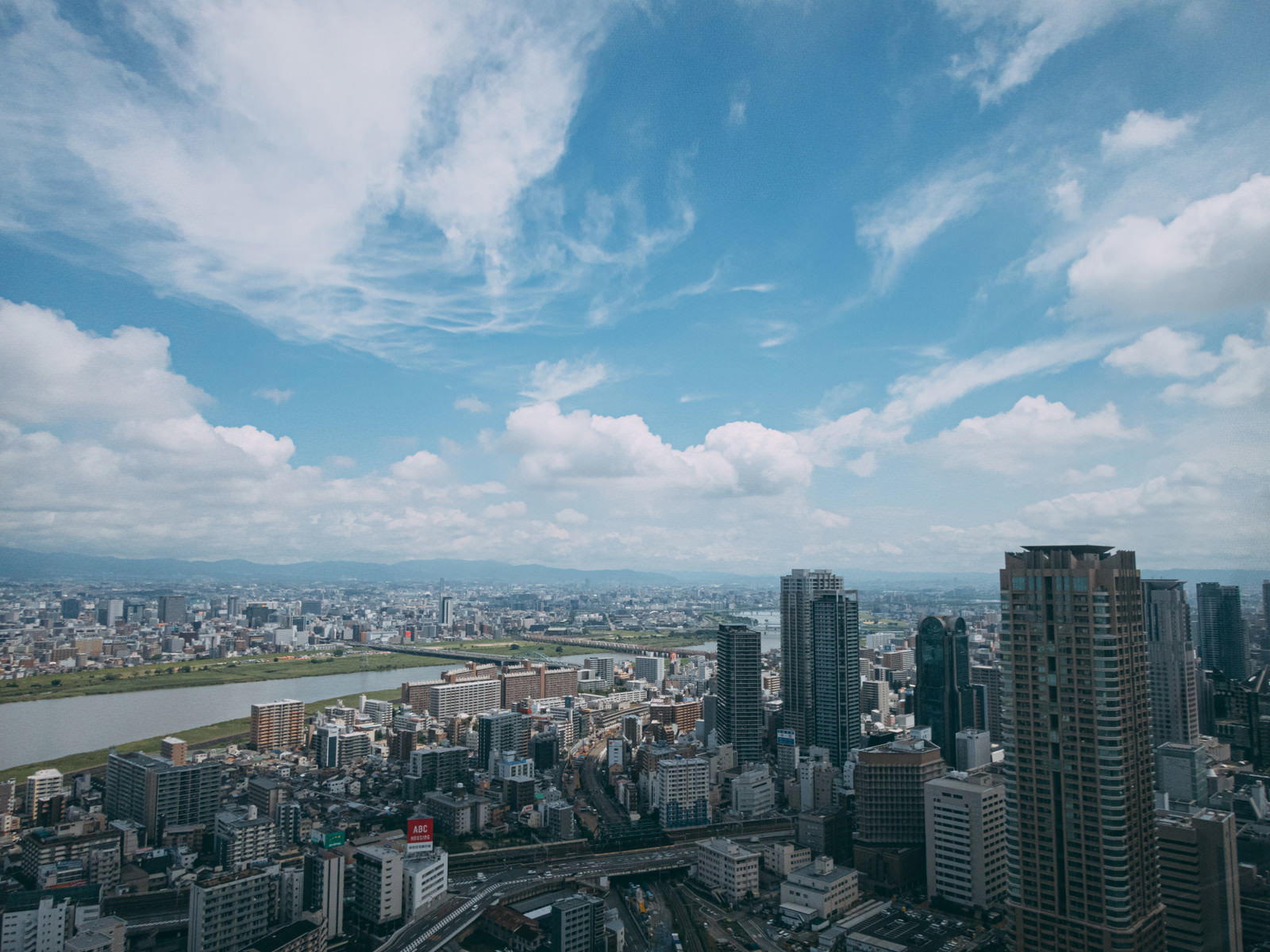 青空と雲が広がる空の下、淀川の流れと大阪梅田の高層ビル群が見渡せる都市景観