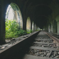 どこまでも続く石造りアーチのトンネルと廃線の線路の写真