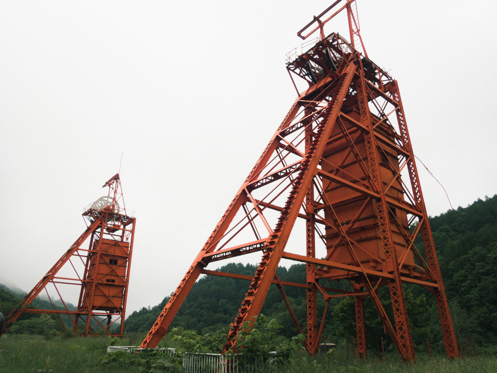 曇り空の下に立つ赤い鉄骨構造の立坑巻上櫓2基