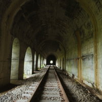 日が差し込む廃線のトンネル内に残るレールと枕木の写真