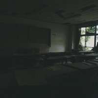 窓から日が差し込む机の並んだ廃屋の古い教室の写真