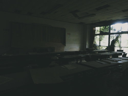 窓から日が差し込む机の並んだ廃屋の古い教室