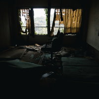 カーテンの隙間から照らされる瓦礫まみれの椅子の写真