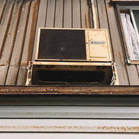 外壁に設置された古いエアコンの室外機と錆びた鉄板の写真