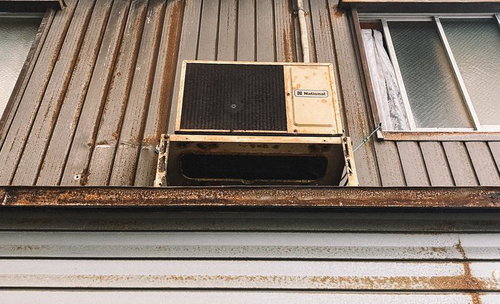 外壁に設置された古いエアコンの室外機と錆びた鉄板