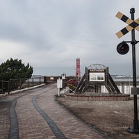 曇り空の下、筑後若津駅跡に立つ記念碑と踏切信号の写真