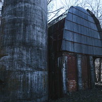 錆びついた円筒形サイロと煉瓦造りの廃工場建屋の写真