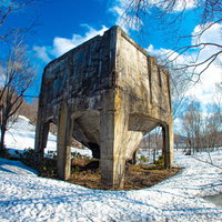 青空の下、残雪に覆われた廃工場と裸木が立つ冬の産業遺産の写真