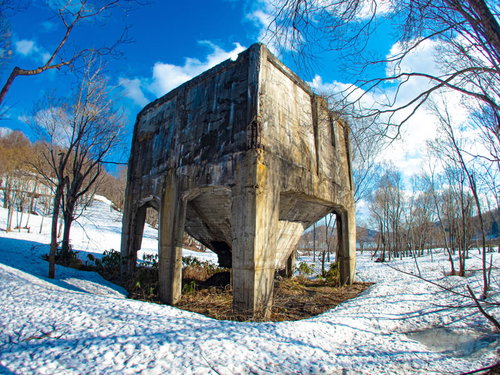 青空の下、残雪に覆われた廃工場と裸木が立つ冬の産業遺産