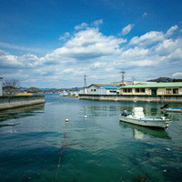 青空と白い雲が広がる尾道の百島の港と停泊する小型漁船の写真