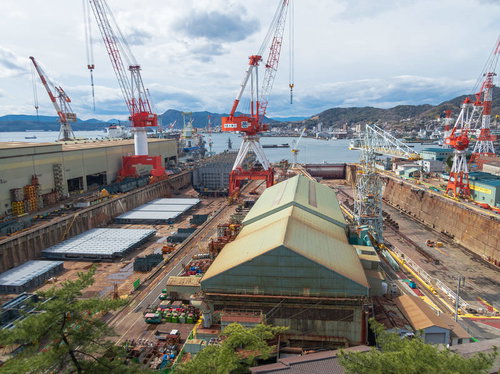 呉市造船所の赤いクレーン群と建造中船舶の空撮風景