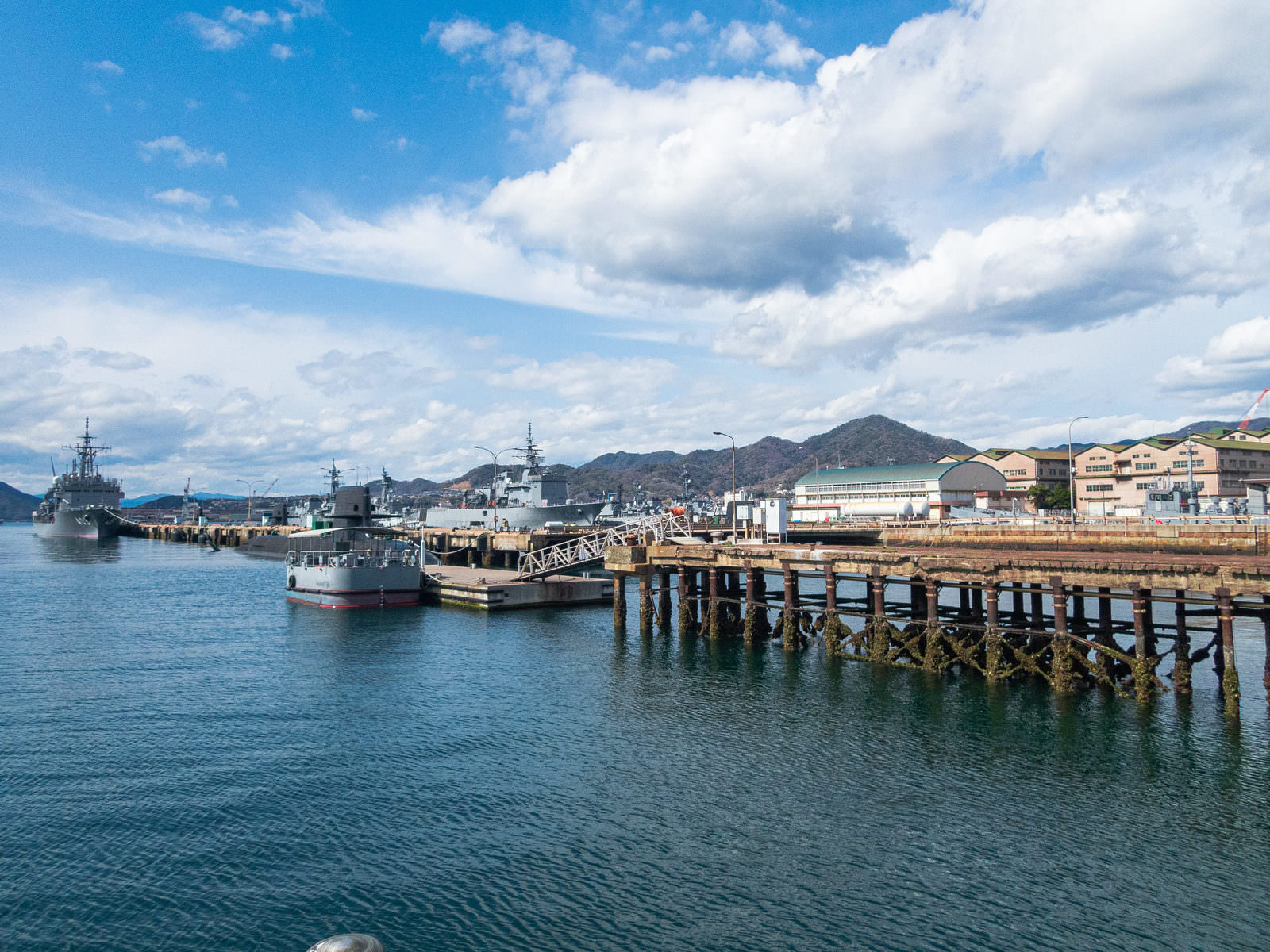 青空の下で自衛隊の軍艦が停泊する港と木製桟橋の風景
