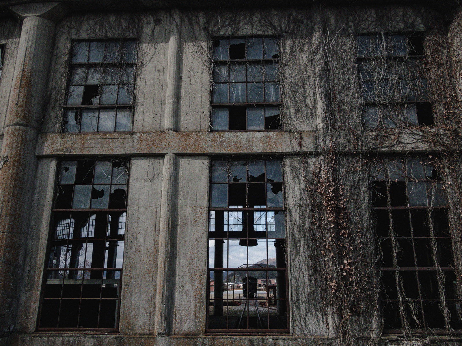 蔦に覆われたコンクリート壁の割れた窓が並ぶ鉄道施設