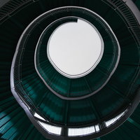 緑色の螺旋階段をのぼる円形ループ構造の建築空間の写真