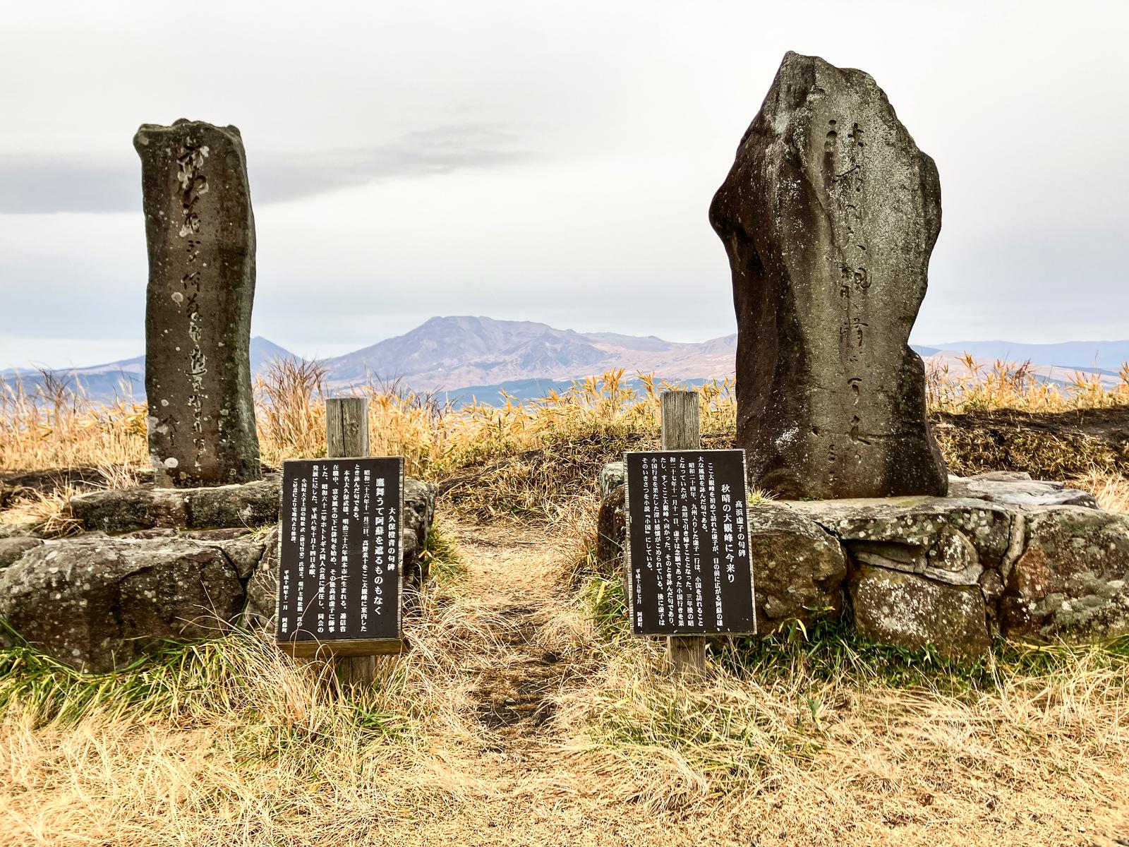 Poetry monuments (kuhi) of Takahama Kyoshi and Okubo Tōsei standing at the summit of Daikanbo Peak, with the Aso mountain range in the background