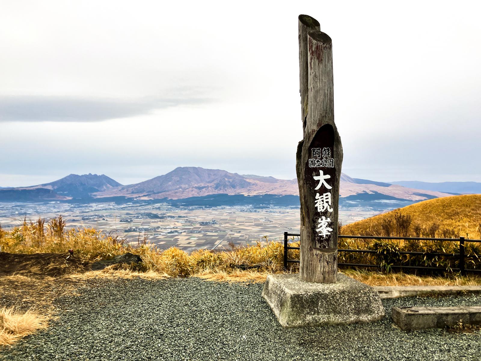 阿蘇国立公園大観峰の木製標柱と、遠方に広がる阿蘇の山並みと田畑