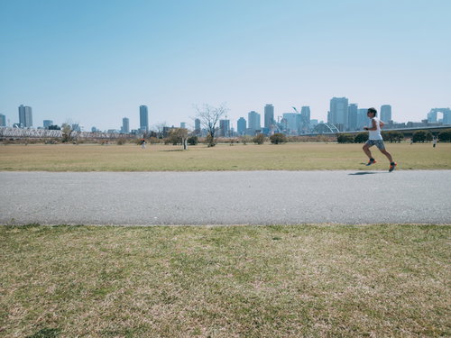 河川敷を走るランナーと都市の高層ビル群を背景に疾走する男性