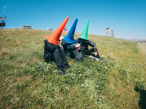 河川敷で語り合う赤・青・緑のカラーコーン三兄弟