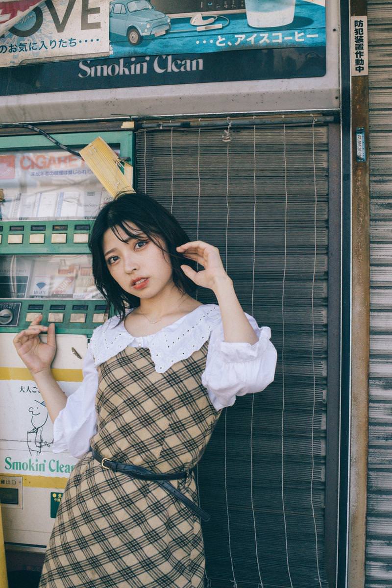 飾磨名店街の閉じた廃たばこ屋の前で、ベージュチェックのジャンパースカートを着た女性が立っている［モデル：高尾実生］