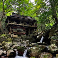 渓谷の流れを眺める廃墟旅館、岩に囲まれた木造二階建ての古民家の写真