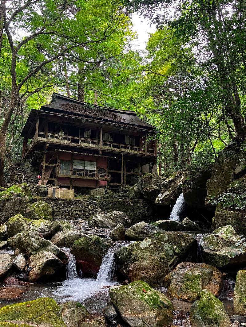 渓谷の流れの前に建つ古い二階建ての廃墟旅館と周囲の森